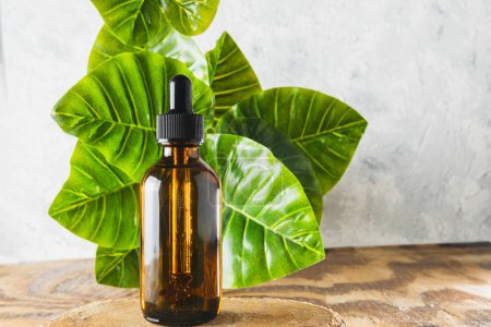 Photo for Amber dropper bottle of essential oils in front of a green leaves background with copy space - Royalty Free Image