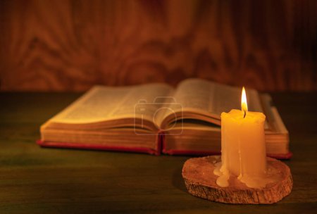 Close-up of a lit candle with a bible on a wooden background. Bible or book concept