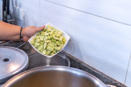 Téléchargez les photos : Womans hand placing beans as an ingredient of the fanesca in a pot in the kitchen. High quality photo - en image libre de droit