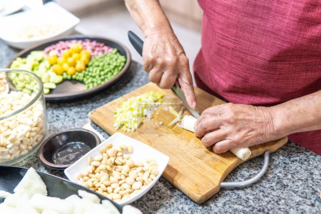 Téléchargez les photos : Hands of an elderly woman cutting onions with several legumes. High quality photo - en image libre de droit