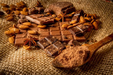 Stillleben verschiedener Schokoladensorten mit Mandeln und Gewürzen wie Sternanis und Nelken auf einem Sack