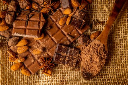 Overhead shot of chocolate pieces of different varieties with almonds and spices on a rustic background