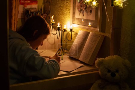 Foto de A Ukrainian schoolgirl does her homework by candlelight during a blackout during the Russian-Ukrainian war - Imagen libre de derechos