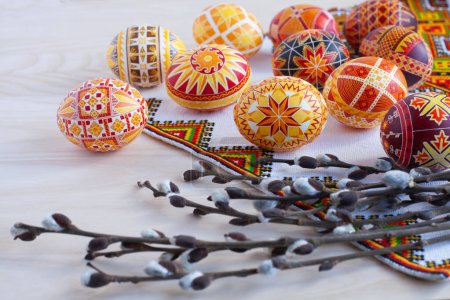 bunte traditionelle ukrainische Ostereier und Weidenzweige auf dem Hintergrund eines bestickten Handtuchs und eines Holztisches
