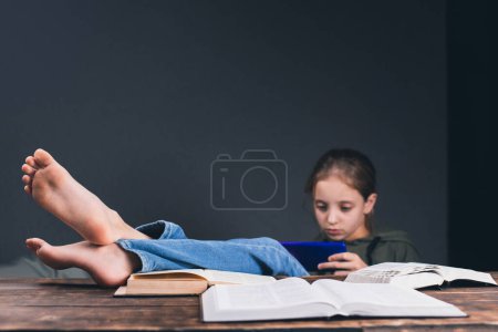 A girl with a phone in her hands. The girl plays on the phone, ignoring books and studies. Open books on the table