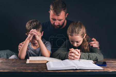 Vater und Kinder beten. Eine offene Bibel auf dem Tisch. Eine Gruppe von Christen betet. Im Raum
