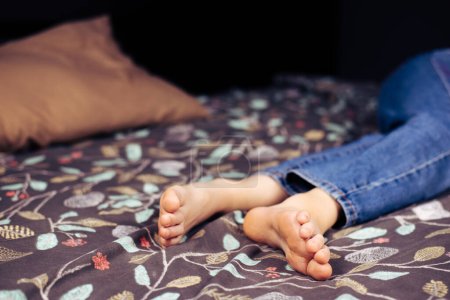Foto de Chica de pies desnudos. Una chica en jeans con los pies desnudos está acostada en la cama. Piernas y pies - Imagen libre de derechos