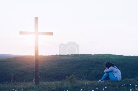 Wooden cross on the background of the sky. The girl is kneeling and praying. Prayer to God. Request for forgiveness of sins. Crucifix. Repentance