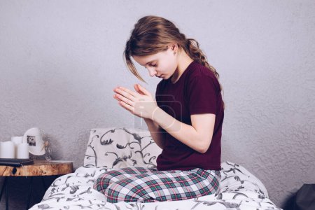 Photo for Teenage girl in pajamas on the bed. Pray on your knees with folded hands. Prayer. - Royalty Free Image