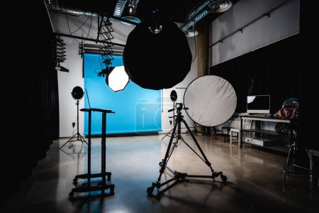 Foto de Interior de un amplio estudio de fotos moderno con proyector de fondo azul colgante y portátil antes de disparar - Imagen libre de derechos