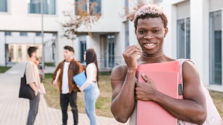 Afrikanische Transgender-Person lächelt in die Kamera, die auf einem Universitätscampus steht