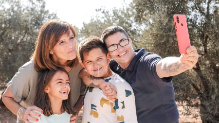 Bonne famille non normative prenant selfie lors d'une excursion dans une zone rurale