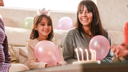 Fille souffler les bougies sur son gâteau d'anniversaire assis sur un canapé avec sa famille