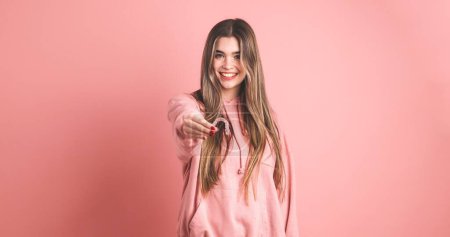 Happy young female model with long blond hair looking at camera while showing an invisible silicone aligner for dental correction over pink background