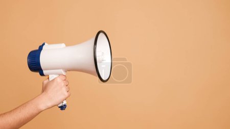 Crop anonymous hand of activist holding white megaphone in studio over brown background with copy space