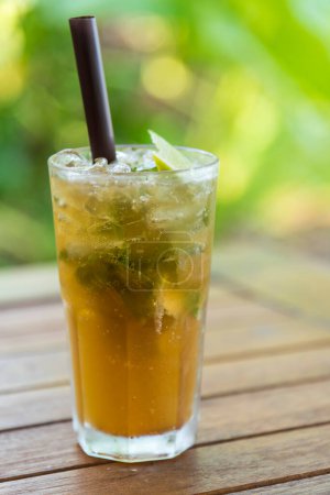 Photo for Lime iced tea with mint, black tea with lime juice and sugar,garnished with lime slices and mint in glass on wood table, nature background, a healthy summer drink. - Royalty Free Image