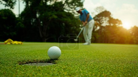 Golfista poniendo pelota en el golf verde, destello de la lente en la hora de la tarde puesta sol. Acción del golfista para ganar después de mucho tiempo poniendo la pelota de golf en el agujero.                               
