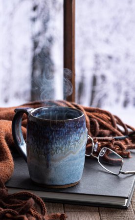 Photo for Steaming hot cup of coffee or tea by a window with snowy winter background - Royalty Free Image