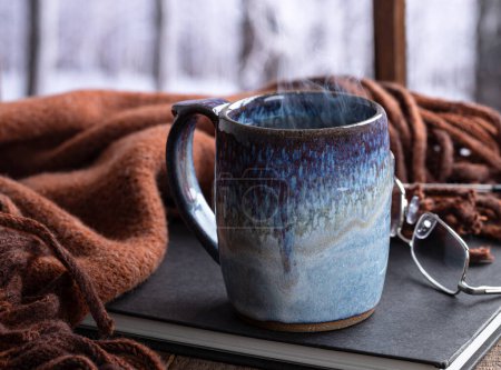 Téléchargez les photos : Tasse chaude de café ou de thé à la vapeur près d'une fenêtre avec fond d'hiver enneigé - en image libre de droit
