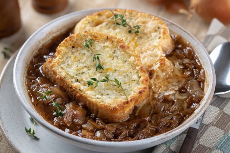 Photo for Closeup of french onion soup with toasted cheese baguette garnished with thyme on a rustic wooden table background - Royalty Free Image