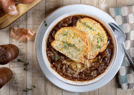 French onion soup with toasted cheese baguette garnished with thyme on a rustic wooden table background, overhead view
