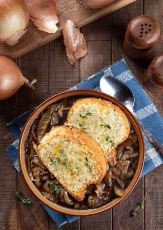 Photo for French onion soup with toasted cheese baguette garnished with thyme on a rustic wooden table background - Royalty Free Image