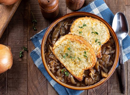Photo for French onion soup with toasted cheese baguette garnished with thyme on a rustic wooden table background - Royalty Free Image