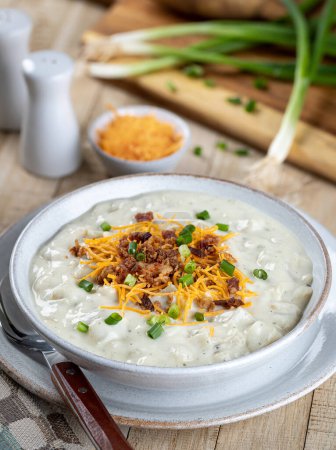 Photo for Creamy potato soup with bacon pieces, shredded cheddar cheese and chopped green onions in a white bowl - Royalty Free Image