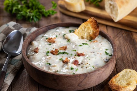 Photo for New england clam chowder with bacon, parsley and toasted french bread in a wooden bowl - Royalty Free Image