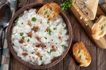 Photo for New england clam chowder with bacon, parsley and toasted french bread in a wooden bowl.  Horizontal overhead view - Royalty Free Image