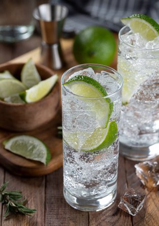Foto de Gin and tonic cocktail with lime slices, and ice on a rustic wooden table - Imagen libre de derechos