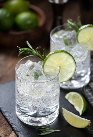 Téléchargez les photos : Cocktail gin tonique avec tranches de citron vert, romarin et glace sur une planche d'ardoise noire - en image libre de droit