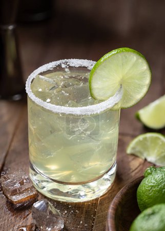 Téléchargez les photos : Margarita cocktail with ice, lime and salt rim on a rustic wooden table - en image libre de droit