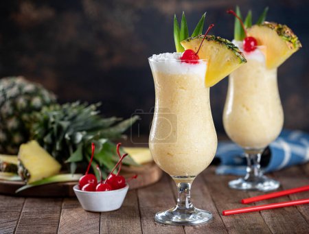 Photo for Pina colada cocktail garnished with cherry, pineapple slice and leaves on a rustic wooden table - Royalty Free Image