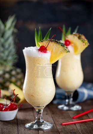 Photo for Pina colada cocktail garnished with cherry, pineapple slice and leaves on a rustic wooden table - Royalty Free Image