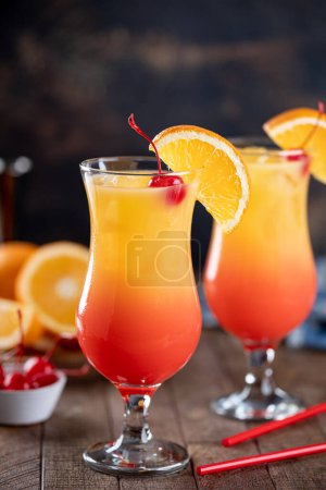 Photo for Tequila sunrise cocktail garnished with cherry and orange slice on a rustic wooden table - Royalty Free Image