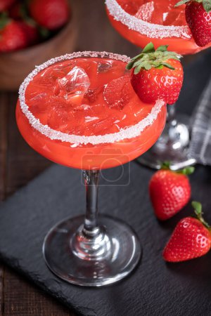 Photo for Strawberry margarita cocktail garnished with strawberries and salt rim on a black slate board - Royalty Free Image