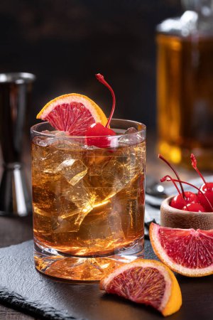 Foto de Cóctel de whisky a la antigua con rodajas de cereza y naranja sobre un fondo rústico de madera - Imagen libre de derechos