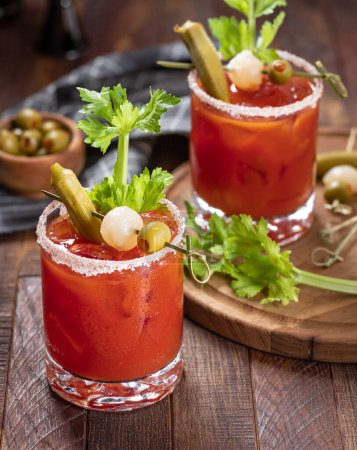 Photo for Bloody mary cocktail garnished with celery, okra, onion, olive and salt rim on a rustc wooden table - Royalty Free Image