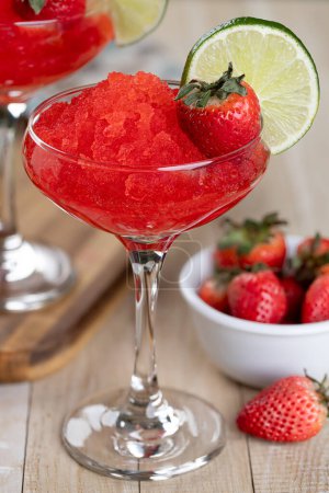Téléchargez les photos : Gros plan de daiquiri aux fraises surgelées garni de fraises et de tranches de lime sur une table en bois - en image libre de droit