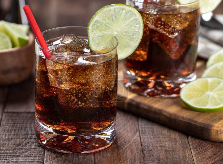 Téléchargez les photos : Cocktail rhum-cola avec tranche de lime sur table rustique en bois. Gros plan - en image libre de droit