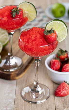 Téléchargez les photos : Daiquiri de fraises surgelé garni de fraises et de tranches de lime sur une table rustique en bois - en image libre de droit