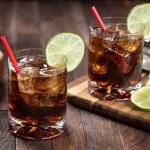 Rum and cola cocktail with lime slice on rustic wooden table