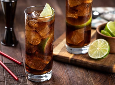 Téléchargez les photos : Cocktail de rhum et de cola dans de grands verres avec tranche de citron vert sur une table en bois rustique - en image libre de droit
