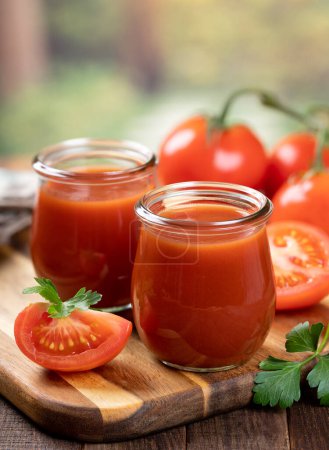 Téléchargez les photos : Jus de tomate dans des bocaux en verre avec des tranches de tomate fraîche sur un panneau en bois avec fond extérieur - en image libre de droit