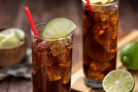 Téléchargez les photos : Cocktail de rhum et de cola dans de grands verres avec tranche de citron vert sur une table en bois rustique - en image libre de droit