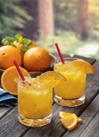 Photo for Orange juice cocktail with orange slices and fresh oranges on old wooden table with nature background - Royalty Free Image