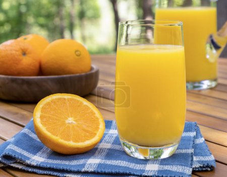 Téléchargez les photos : Verre de jus d'orange et d'oranges à l'extérieur sur une table en bois avec fond nature - en image libre de droit