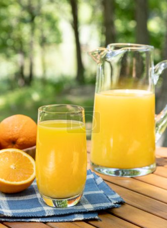 Photo for Glass of orange juice and oranges outdoors on a wooden table with nature background - Royalty Free Image