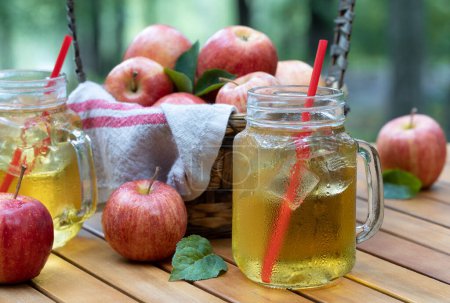 Téléchargez les photos : Jus de pomme froid dans des verres avec des pommes fraîches à l'extérieur sur la terrasse tabe avec fond de nature - en image libre de droit